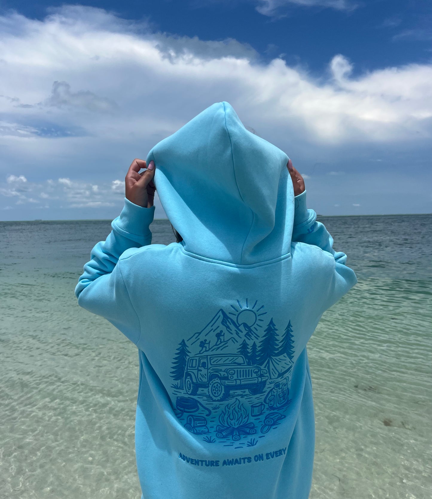 Woman wearing a blue embroidered Summit & Coast mountain hoodie on the beach